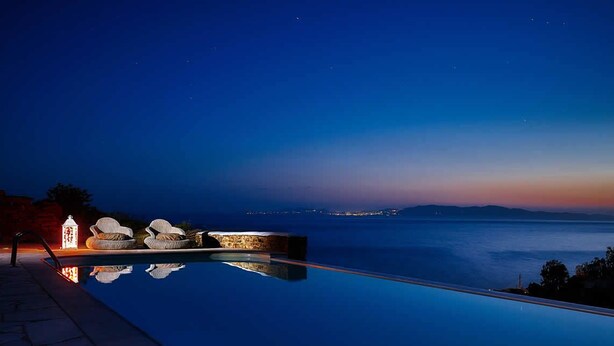 An infinity pool with a view of the sea and city lights at dusk. - Vega Apartments (Tinos)