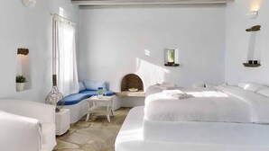 A modern, minimalist bedroom with a large bed, a smaller sofa, and a small table. - Vega Apartments (Tinos)