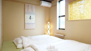 A bedroom with a bed, a wall-mounted air conditioner, a window with blinds, and a decorative wall piece. - Horikawakoji Umenotoan (Kyoto)