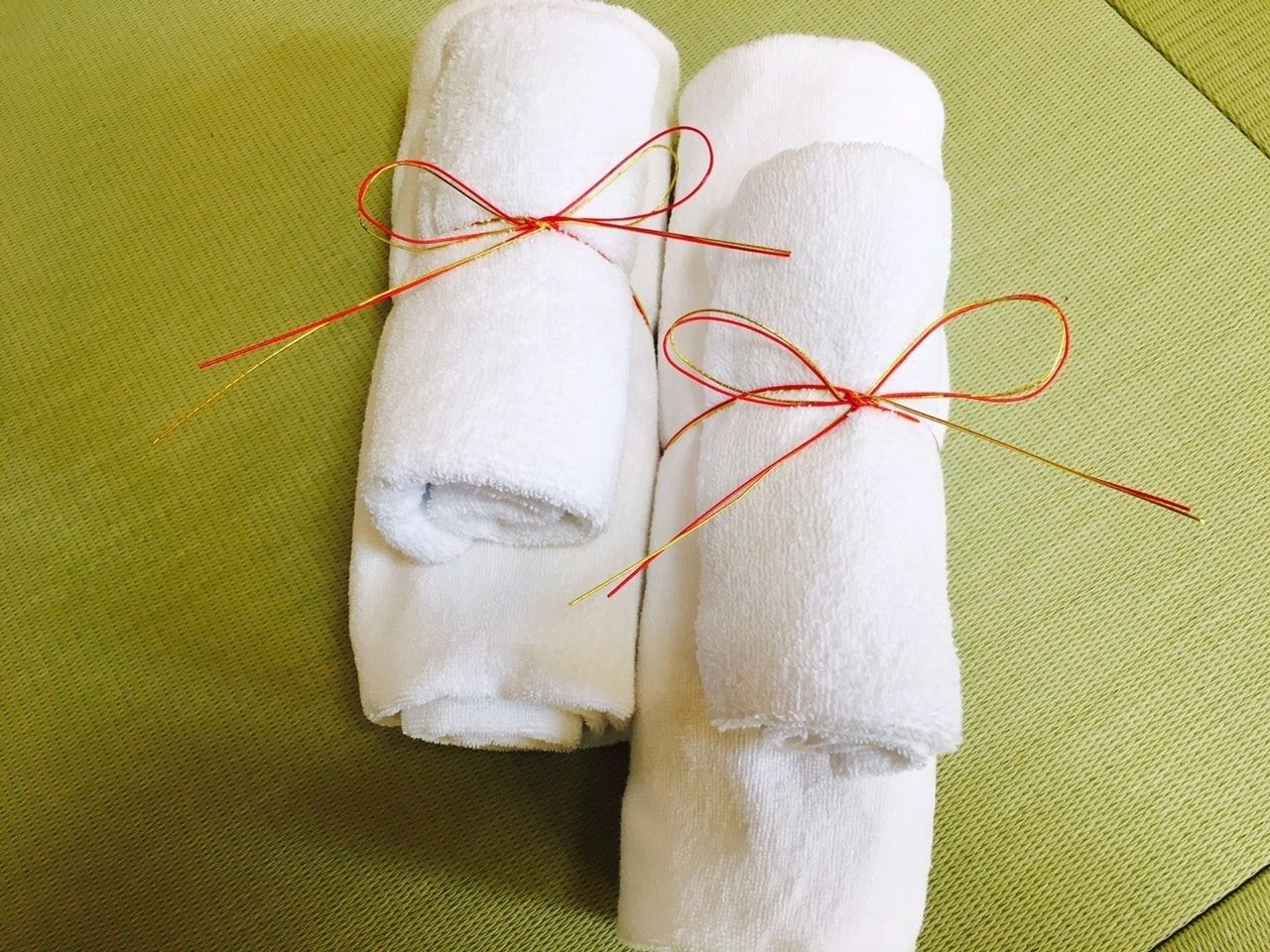 Deux serviettes blanches enroulées et attachées avec des ficelles rouges et jaunes, le tout posé sur un fond en tissu vert.