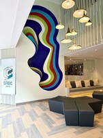 Um hall de hotel moderno com um design de parede abstrato e colorido, luminárias contemporâneas e uma área de estar com bancos acolchoados.
