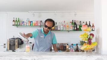 Eine Bar mit einem Barkeeper, der ein Getränk zubereitet, Regalen mit verschiedenen Flaschen und einem Obstkorb.