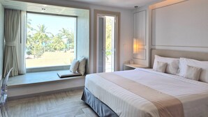 Una habitación de hotel con una cama grande, una ventana con vistas a palmeras, una mesita de noche y un buró.