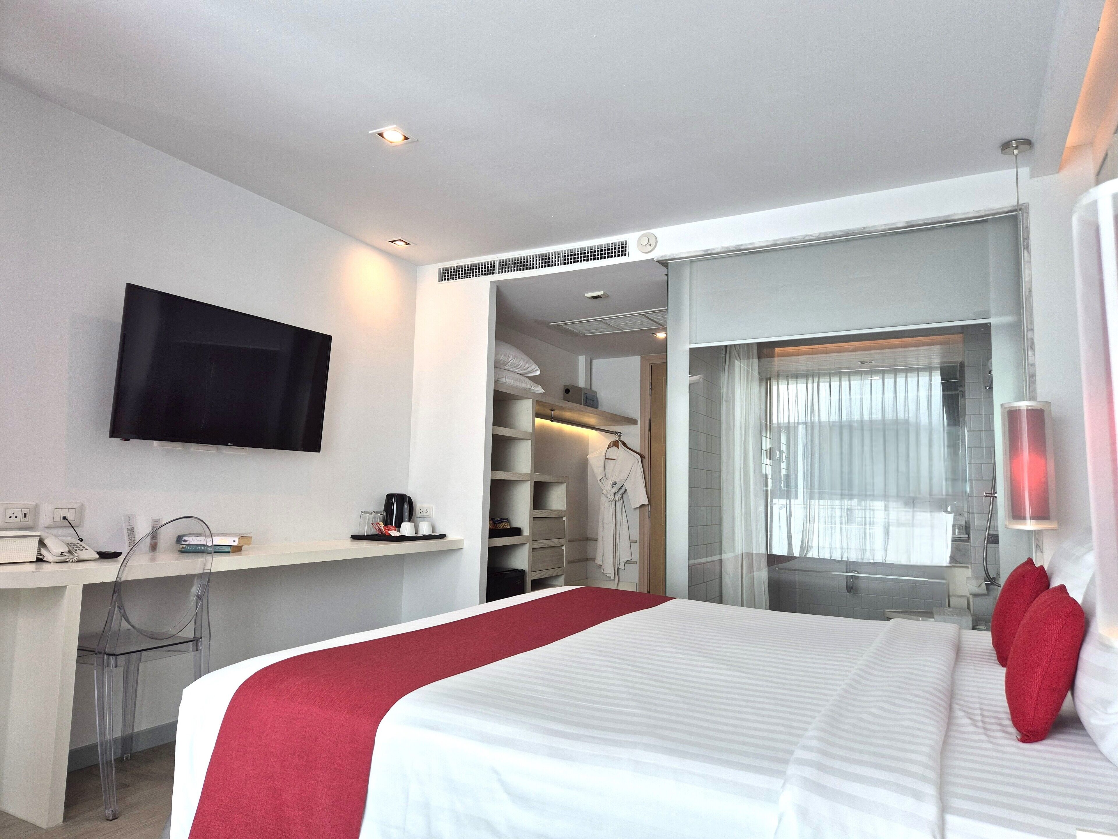 Habitación de hotel con cama, televisión, escritorio con silla, armario y baño con ducha.