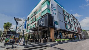 Un edificio moderno con una cafetería en la planta baja, que cuenta con terraza al aire libre y un cielo despejado.