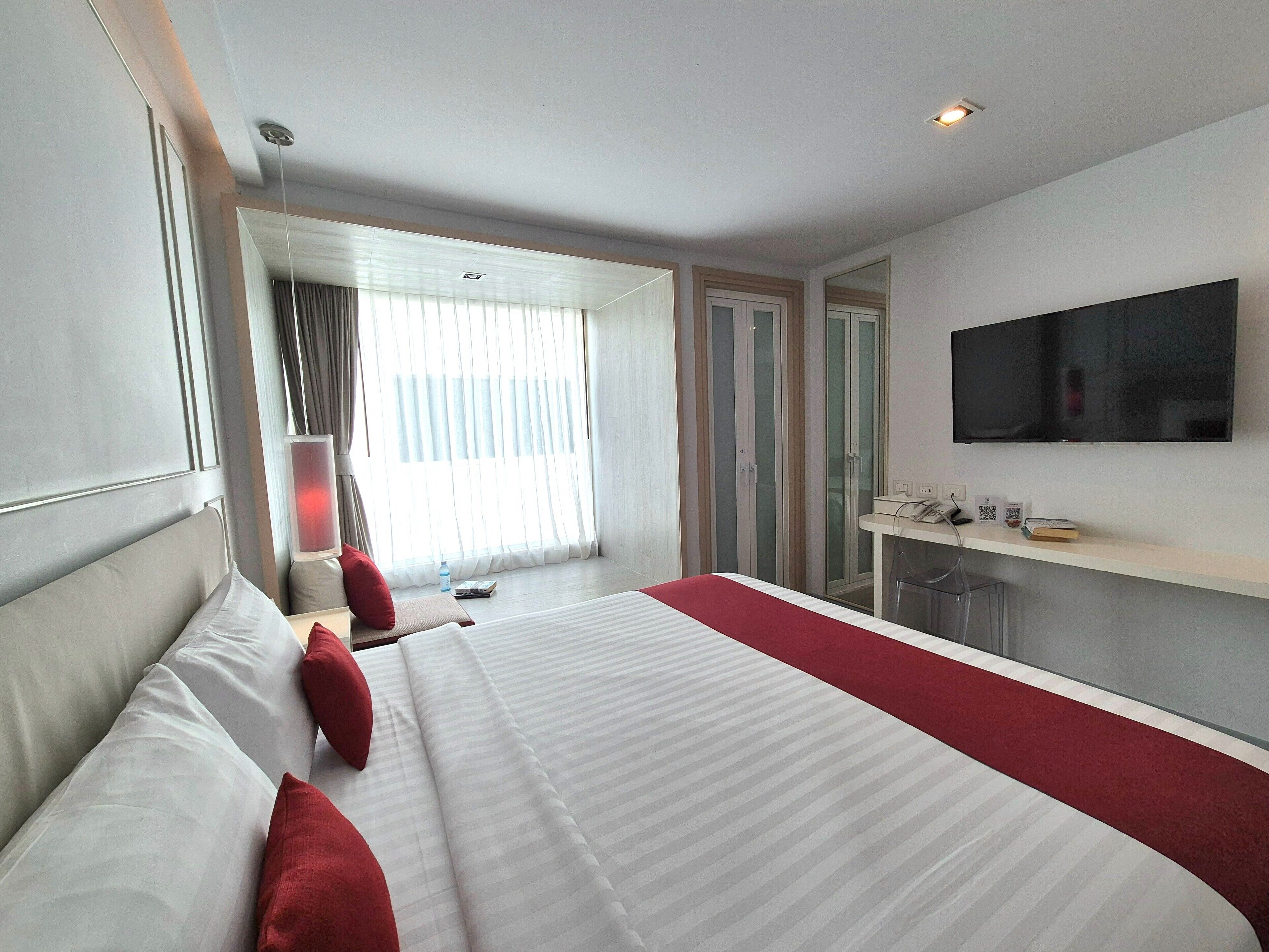 A hotel room with a large bed, a TV mounted on the wall, a bedside table, and a window with curtains.