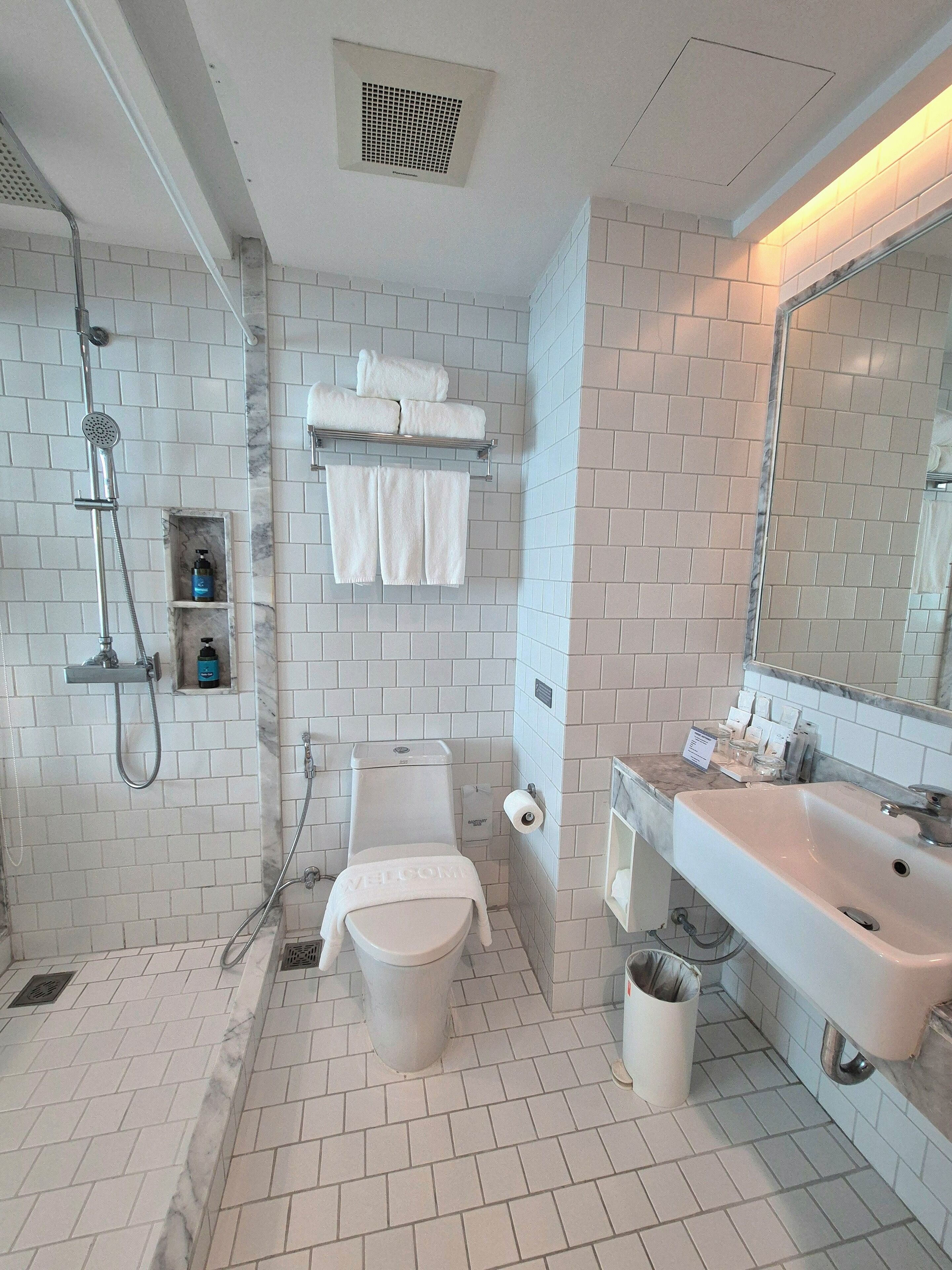 A modern bathroom with white tiles, a shower, a toilet, a sink, and a mirror.