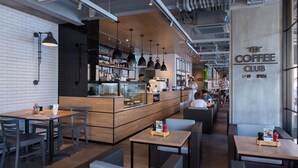 Interior de una cafetería moderna con mesas de madera, lámparas colgantes negras y un mostrador visible con un menú.