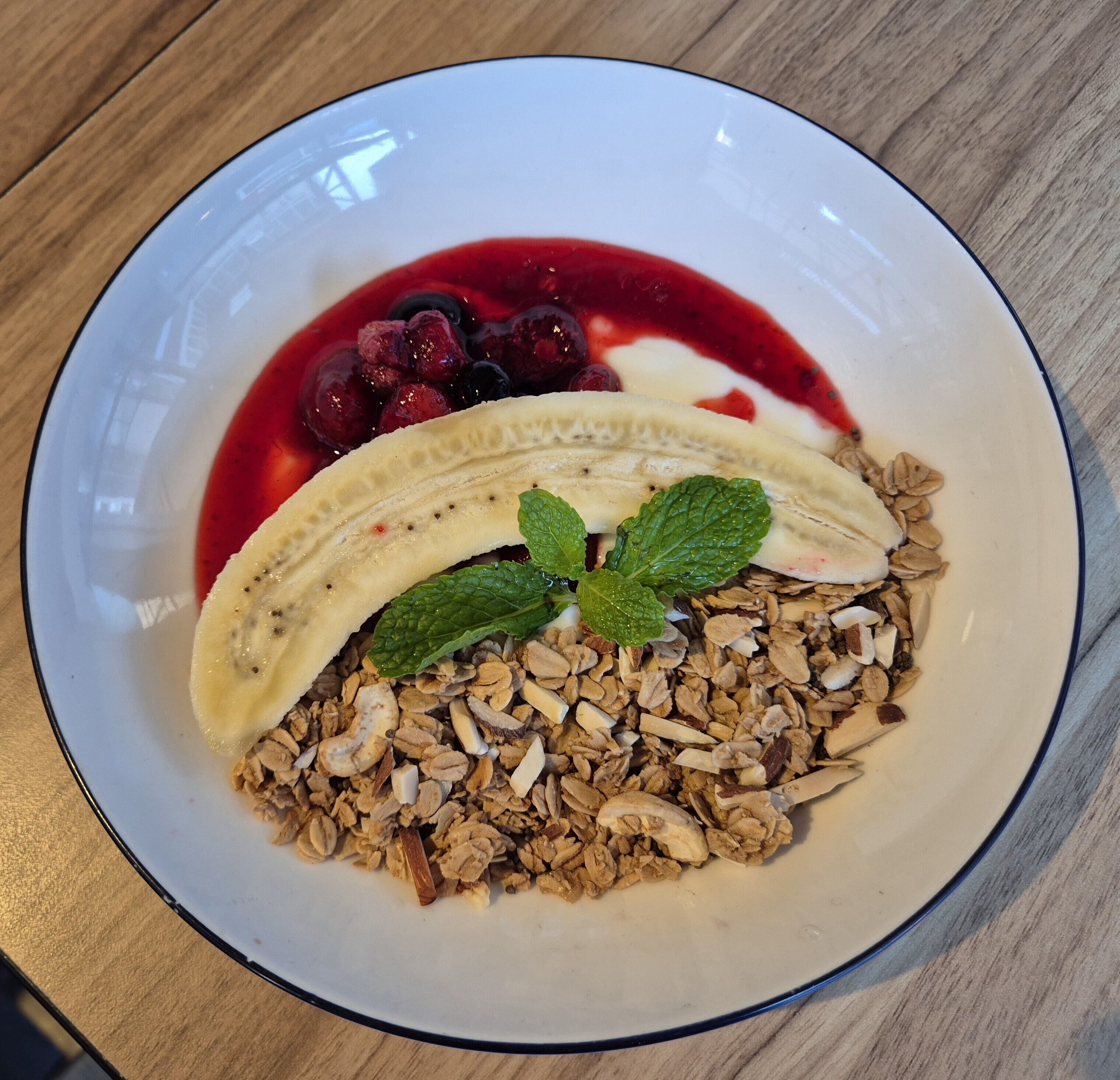 A plate with granola, banana slices, berries, and a mint leaf.