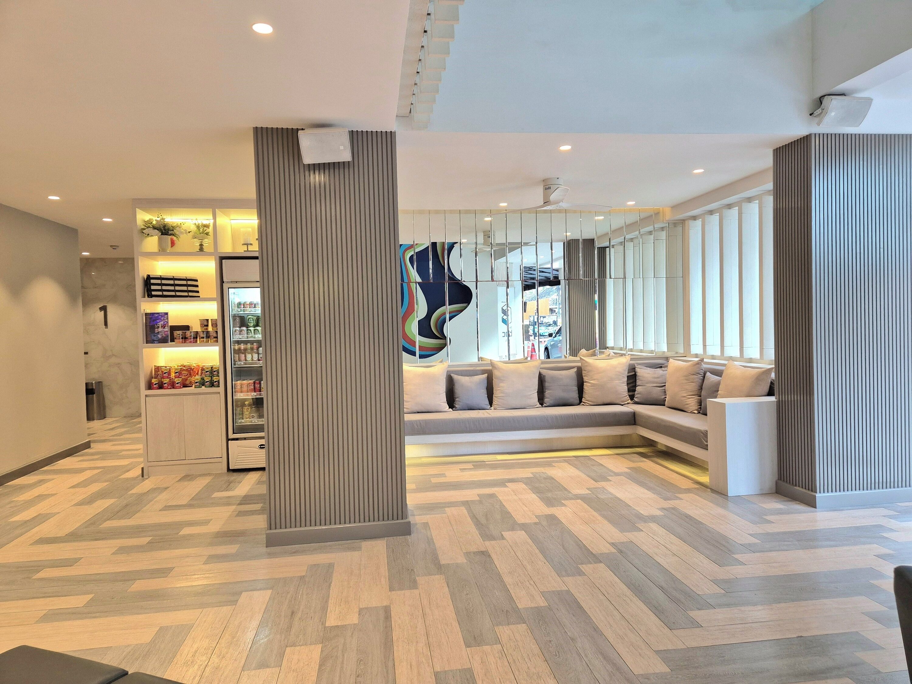 Un moderno vestíbulo de hotel con suelo de patrón espiga, una columna central, una zona de estar con sofá curvo y un cuadro abstracto de gran tamaño.