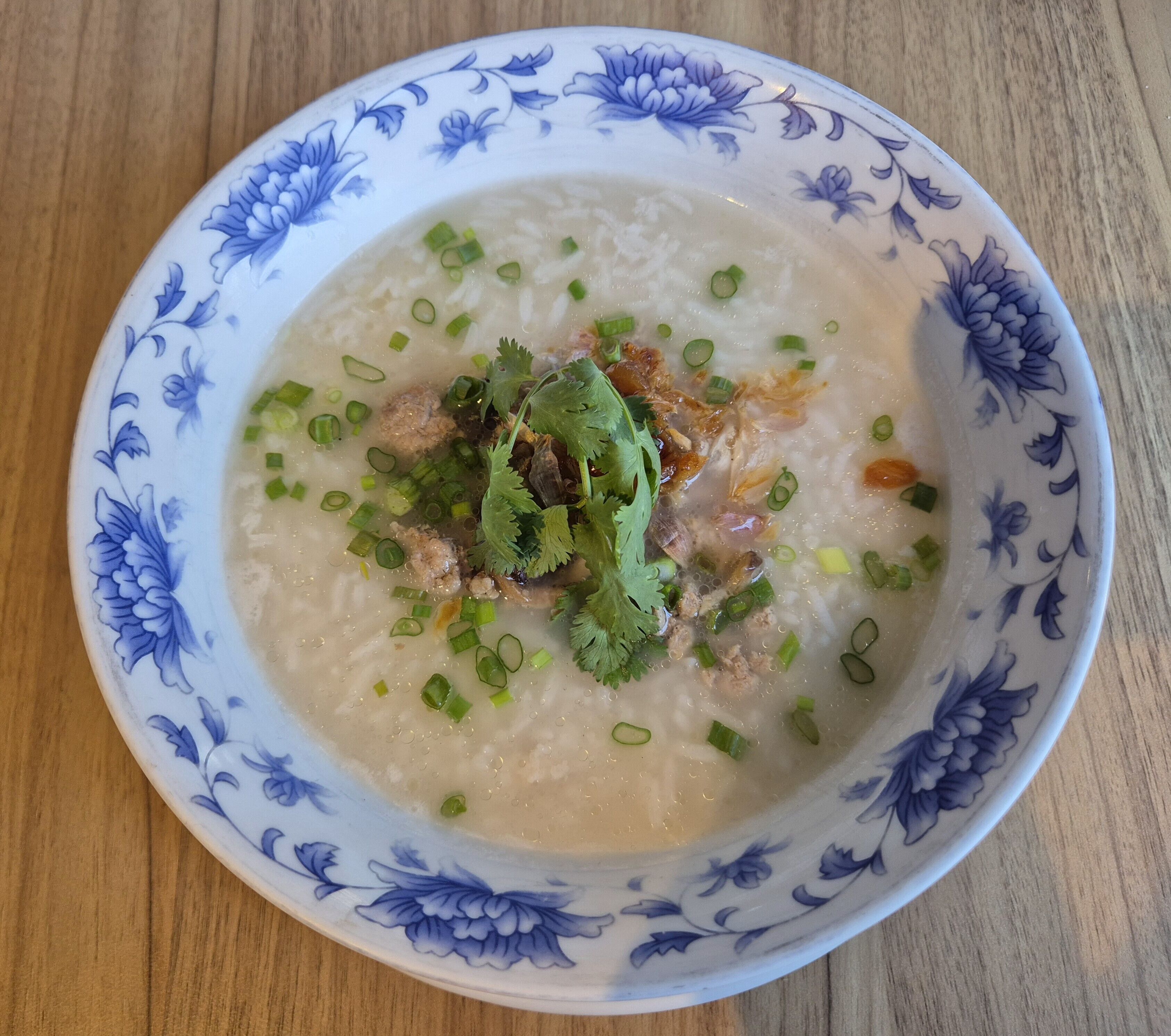 A bowl of congee with green onions and cilantro on a floral-patterned plate.