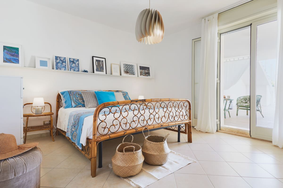Quarto com cama, mesa de cabeceira, abajur e quadros na parede.