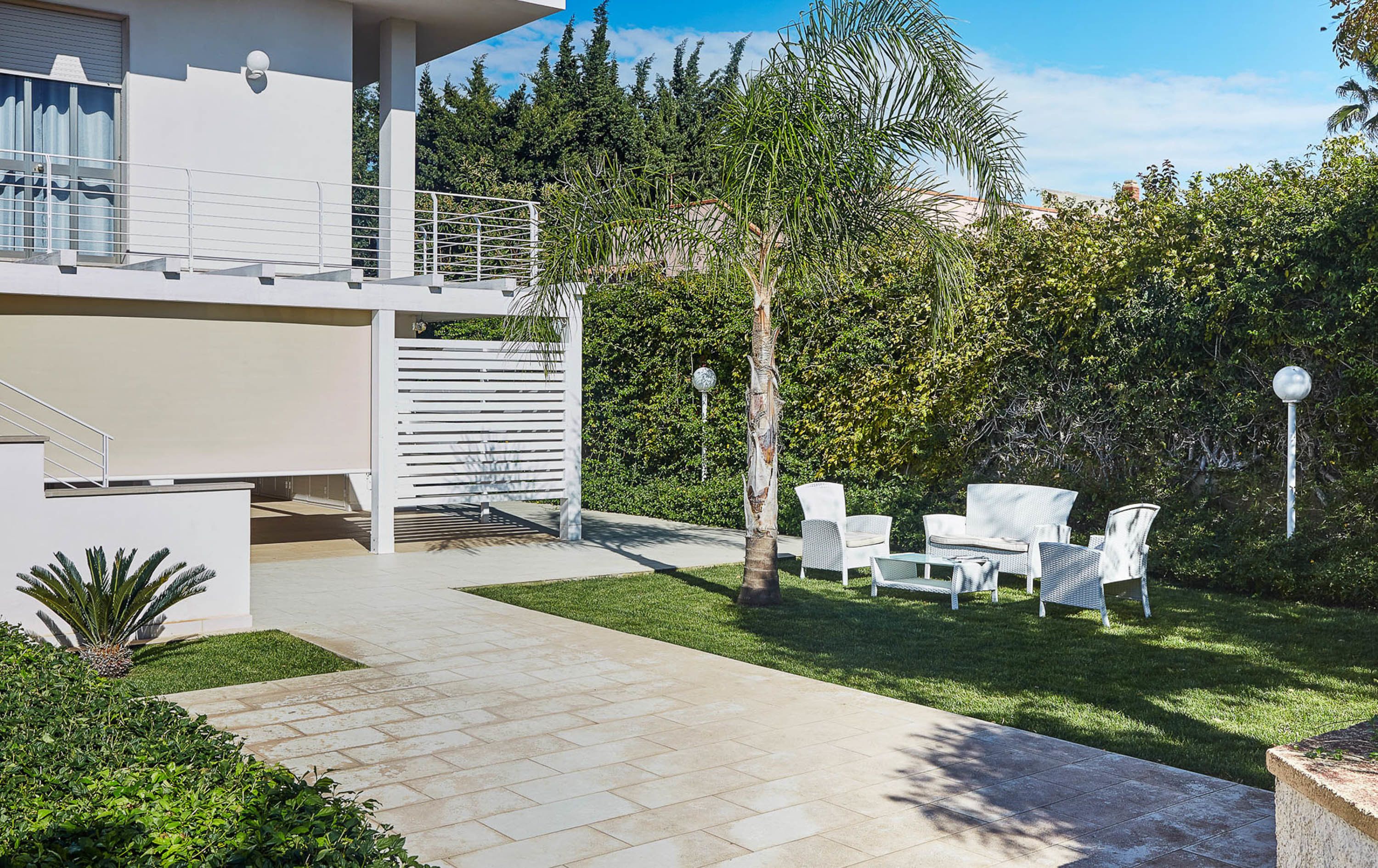 Une terrasse extérieure moderne, avec des meubles en osier blancs, un chemin de pierre et une végétation luxuriante.