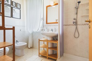 A bathroom with a bidet, sink, mirror, shower, and wooden shelves. - Villa Marina Green CaseSicule (Pozzallo)