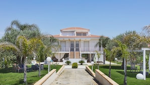 A two-story house with a central staircase, surrounded by a well-maintained garden with palm trees and a clear sky. - Villa Marina Green CaseSicule (Pozzallo)