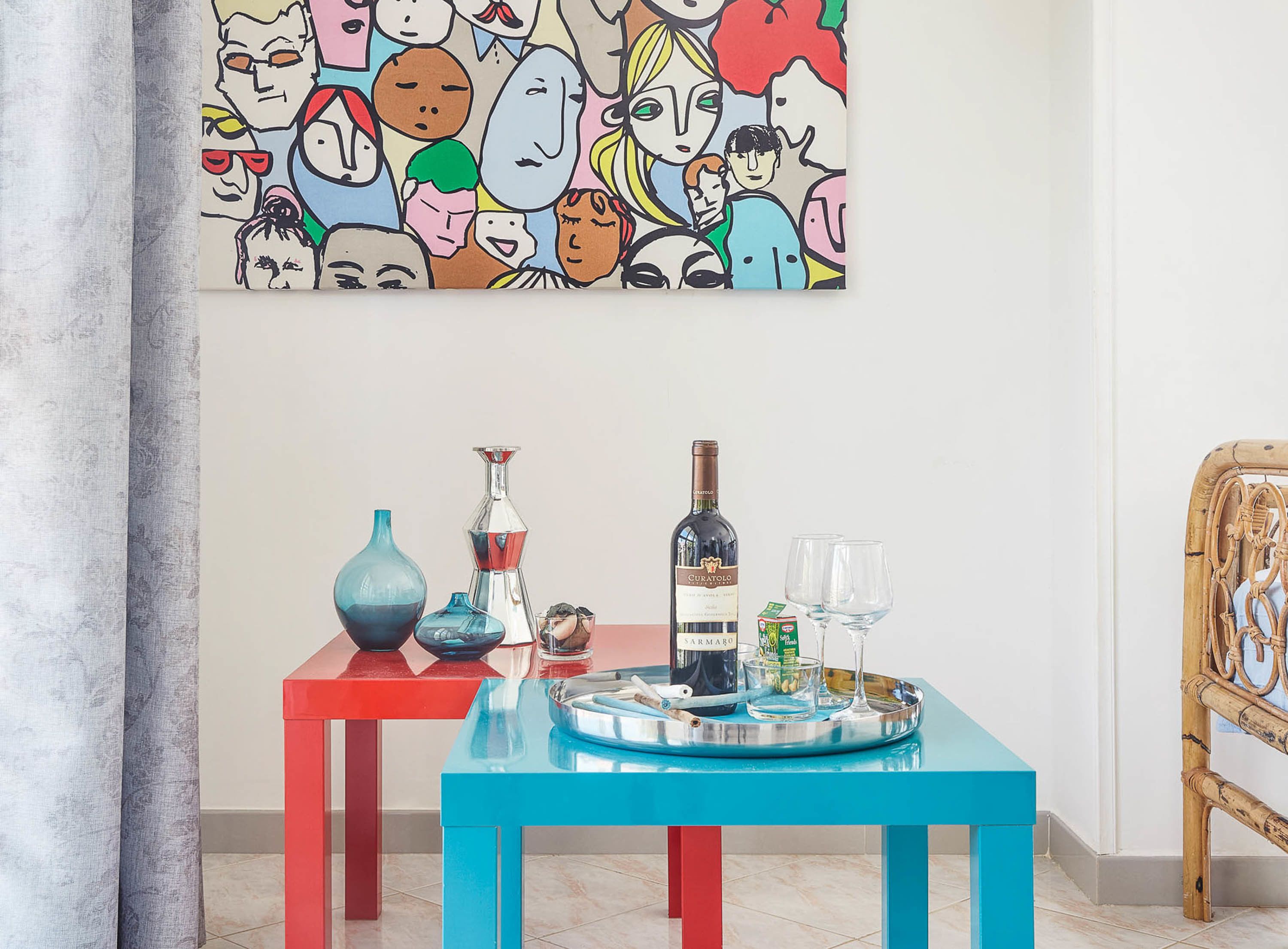 Habitació amb un quadre abstracte i colorit, una taula amb una ampolla de vi, vasos i objectes decoratius.
