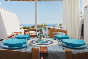 A dining table set with blue plates, a pitcher, and cutlery on a balcony overlooking the sea. - Villa Marina Green CaseSicule (Pozzallo)