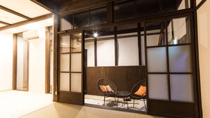 Een traditionele Japanse kamer met tatami vloerbedekking, een lage houten tafel, twee stoelen en een verschuifbaar shoji scherm.