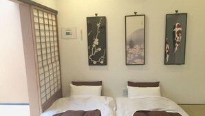 A hotel room with two beds, a shoji screen, and three framed artworks on the wall.