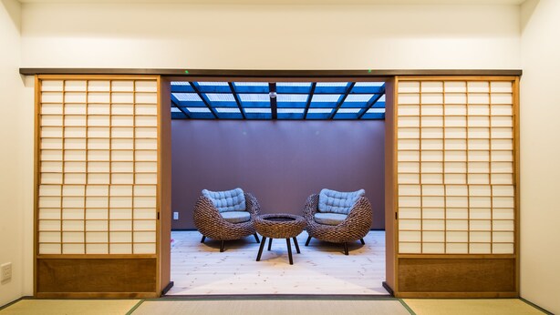 A traditional Japanese room with tatami flooring, a shoji screen door, and two cushioned chairs facing a tatami mat table.