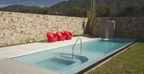 A swimming pool with stone walls, a metal pool ladder, and red chairs along the edge. - Amalinas Hotel (Villa San Lorenzo)