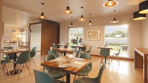 A dining area with multiple tables and chairs, large windows, and hanging pendant lights. - Amalinas Hotel (Villa San Lorenzo)