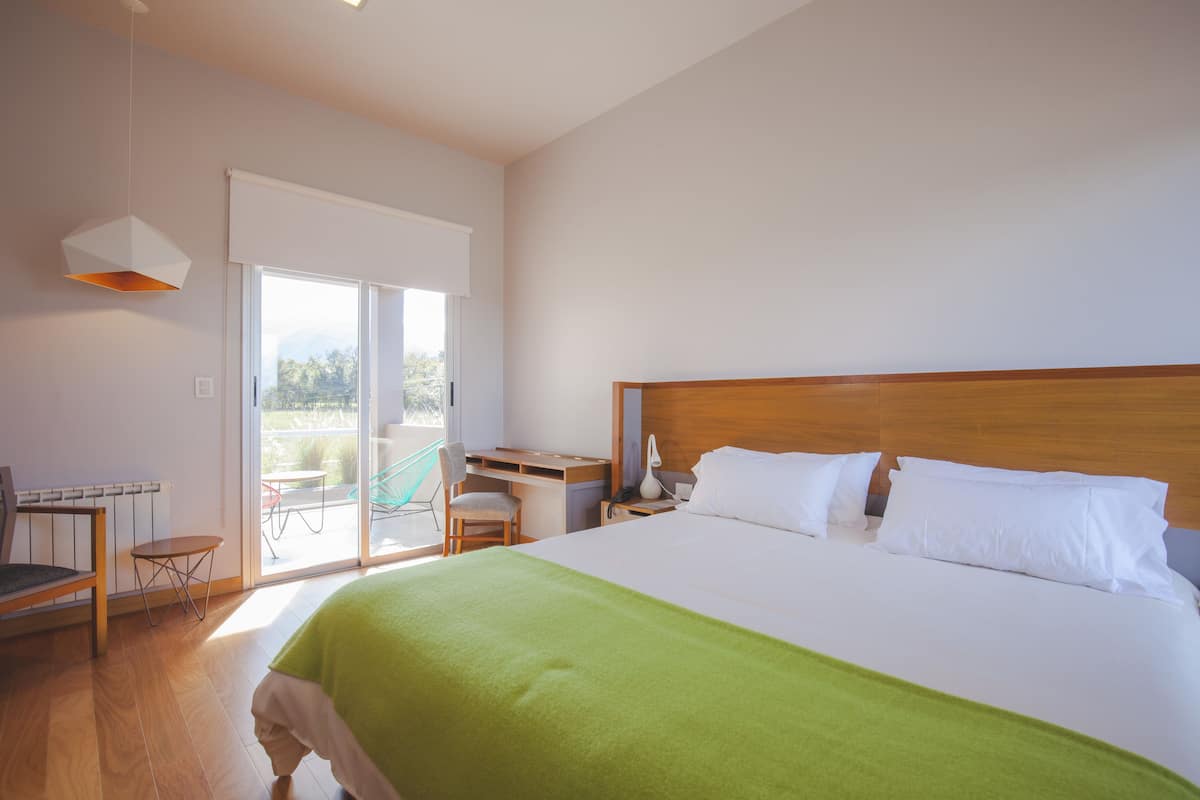 Une chambre d’hôtel avec un grand lit, un bureau et une chaise. Une porte-fenêtre coulissante donne accès à un espace extérieur.