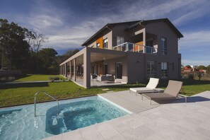 Une maison moderne à deux étages, dotée d’une piscine, d’un espace salon extérieur et d’une pelouse bien entretenue.
