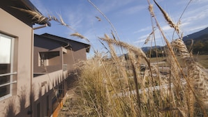 A modern building with a flat roof and large windows, surrounded by tall, dry grass. - Amalinas Hotel (Villa San Lorenzo)