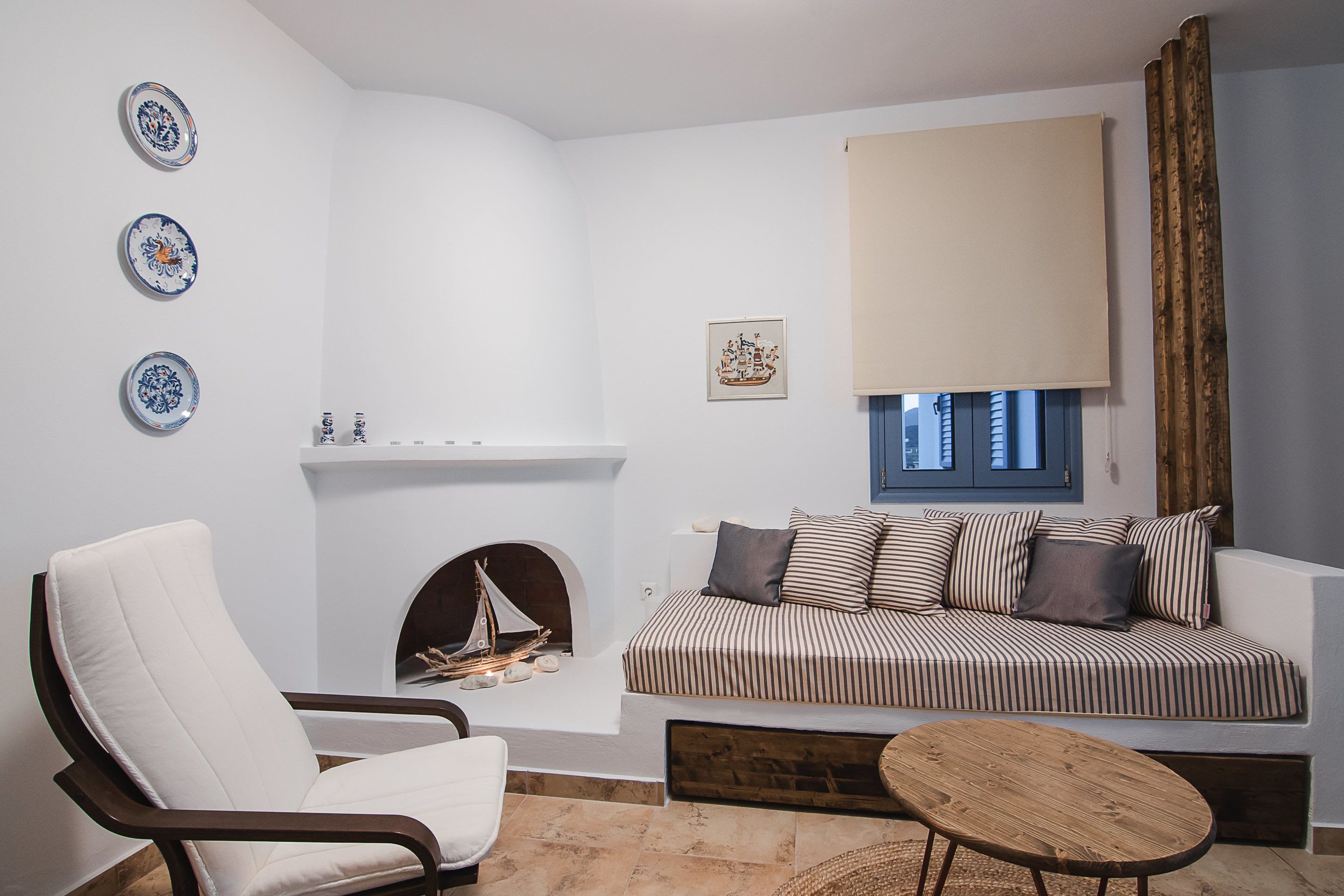 A modern living room with a white sofa, striped cushions, a white armchair, a small fireplace, and decorative plates on the wall.