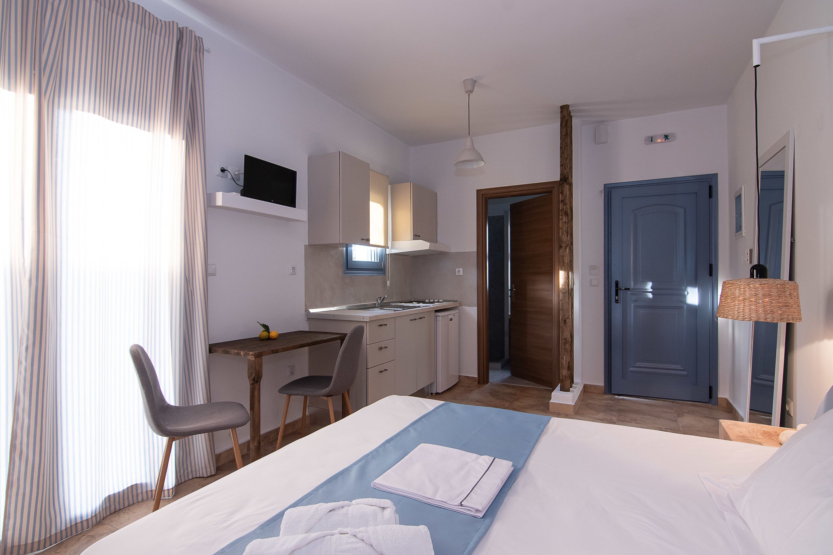 A hotel room with a bed, a desk, a chair, a kitchenette, and a bathroom.