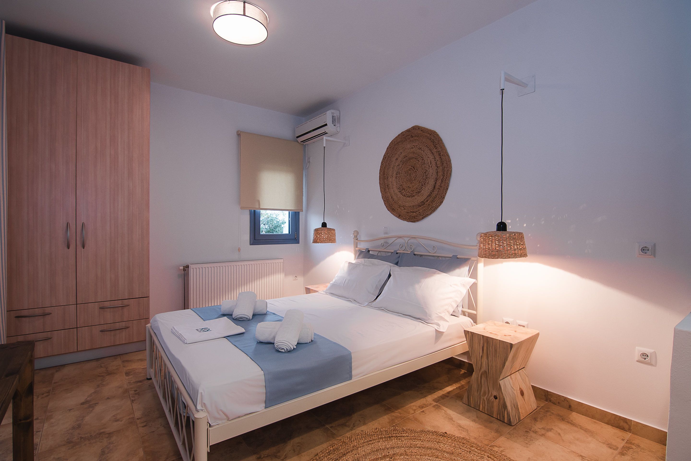 Un dormitorio con cama, mesitas de noche, armario, radiador, ventana y aire acondicionado instalado en la pared.