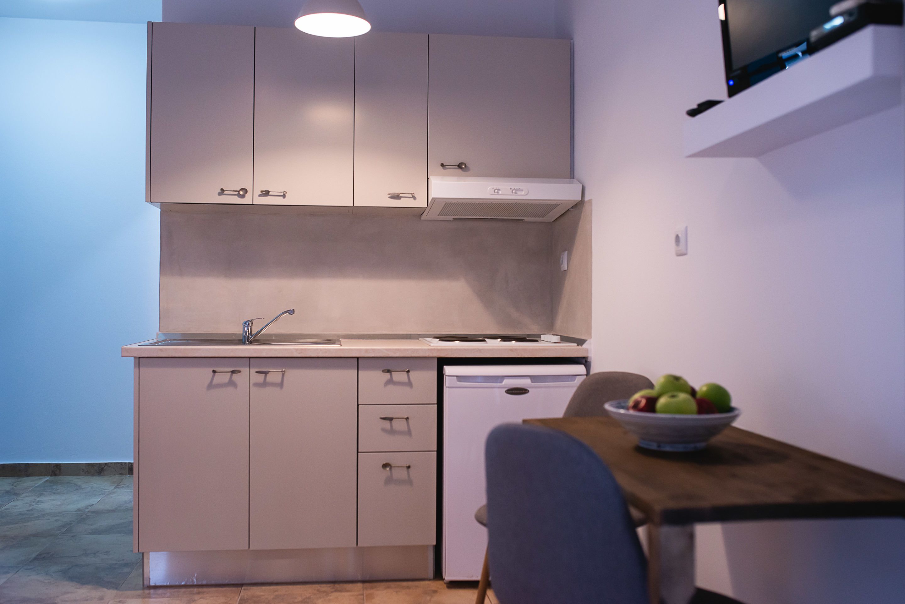 A compact kitchen with white cabinets, a dishwasher, and a dining area with a table and a bowl of fruit.