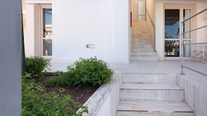 Un bâtiment moderne avec un escalier menant à une porte, le tout entouré de verdure.