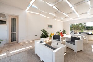 Un patio al aire libre con mobiliario de mimbre blanco, una planta en maceta y vistas del paisaje circundante.
