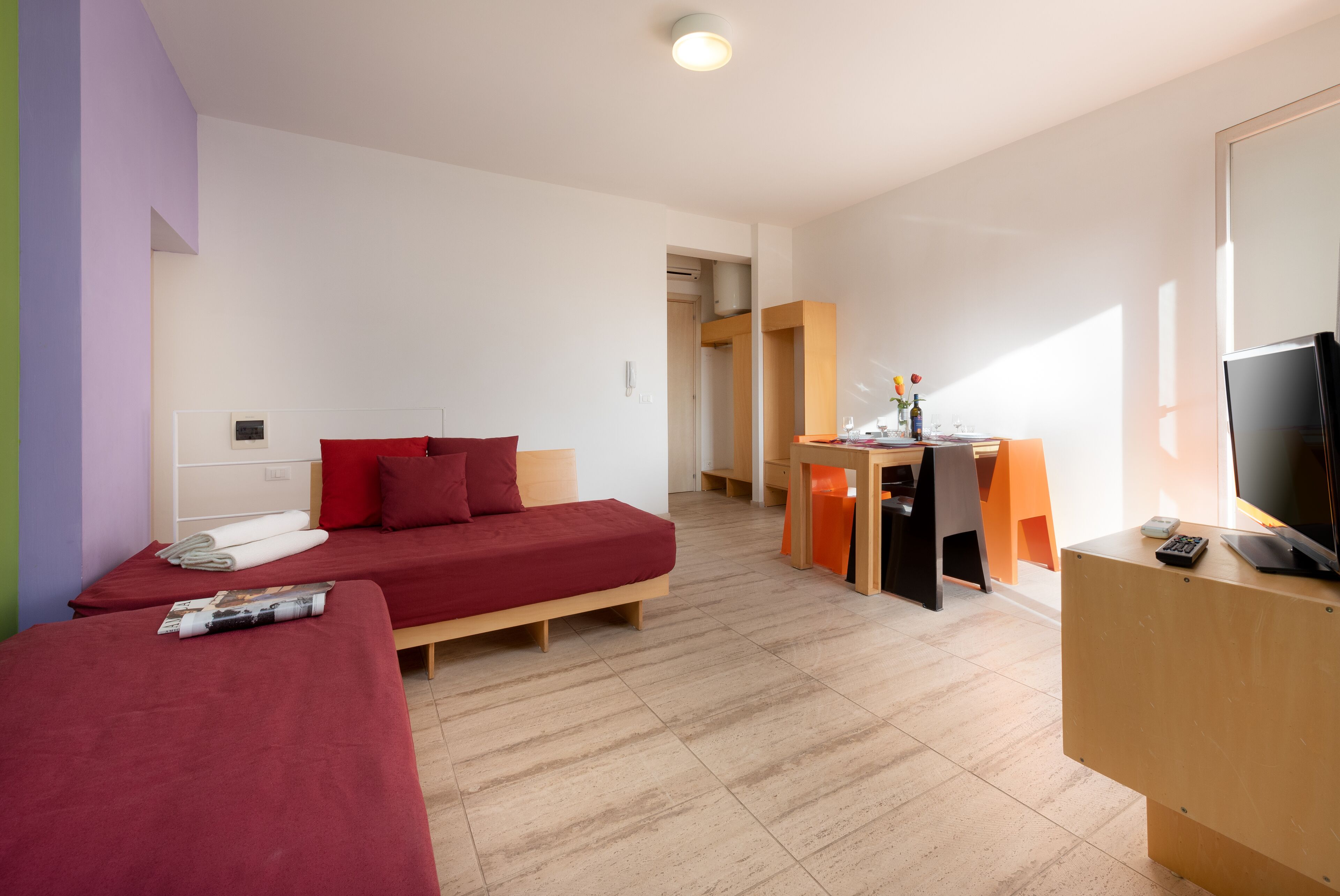 A modern hotel room with a red sofa, a wooden desk, and a television.