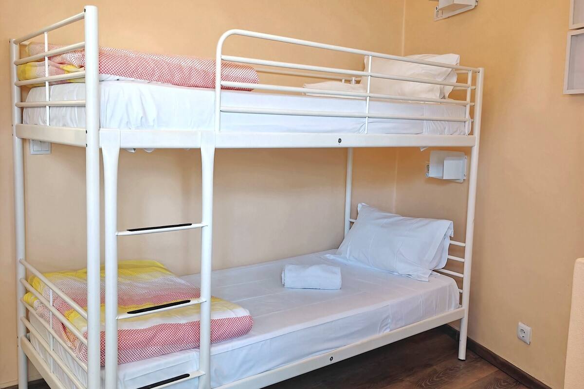 Dormitorio con literas, piso de madera y una silla rosa.