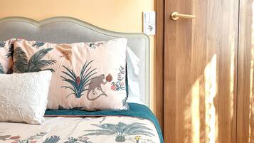 A bed with a tropical-themed duvet, a bedside lamp, and a wooden door with a gold handle.