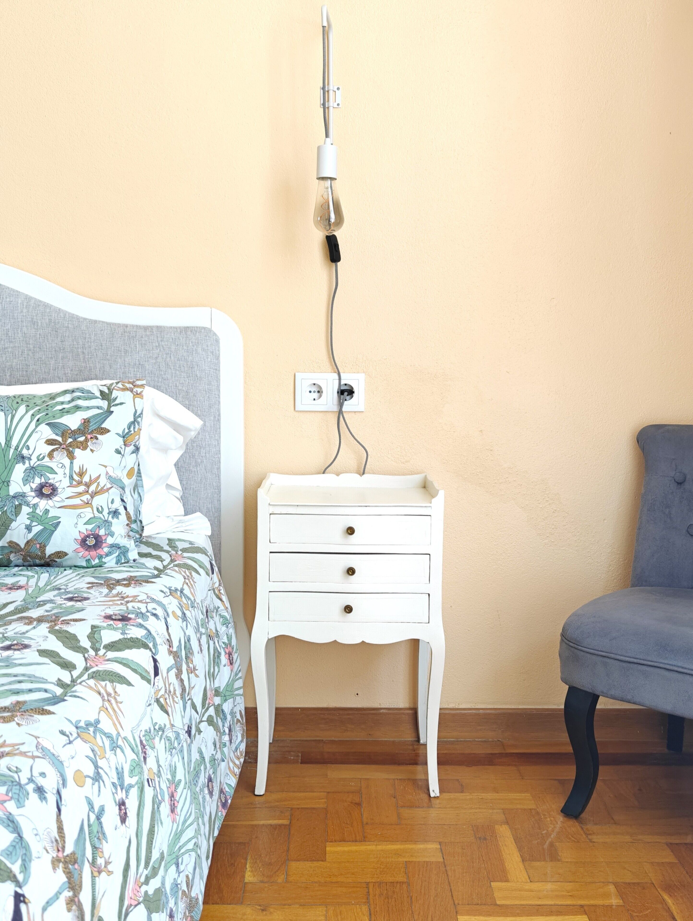 Une chambre à coucher avec un lit, une table de chevet, une chaise et une prise électrique au mur.