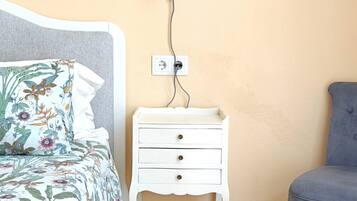 Une chambre à coucher avec un lit, une table de chevet, une chaise et une prise électrique au mur.