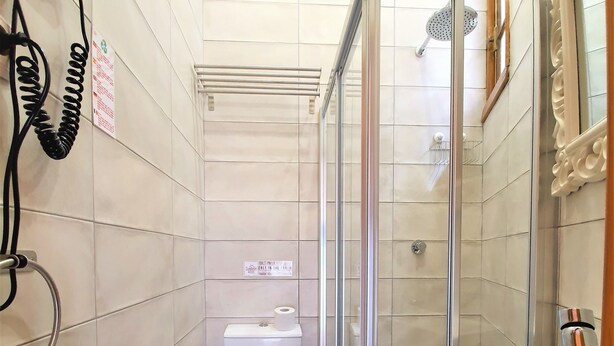 Un baño con inodoro, ducha con puerta de cristal, lavabo y toalla colgada en un perchero.