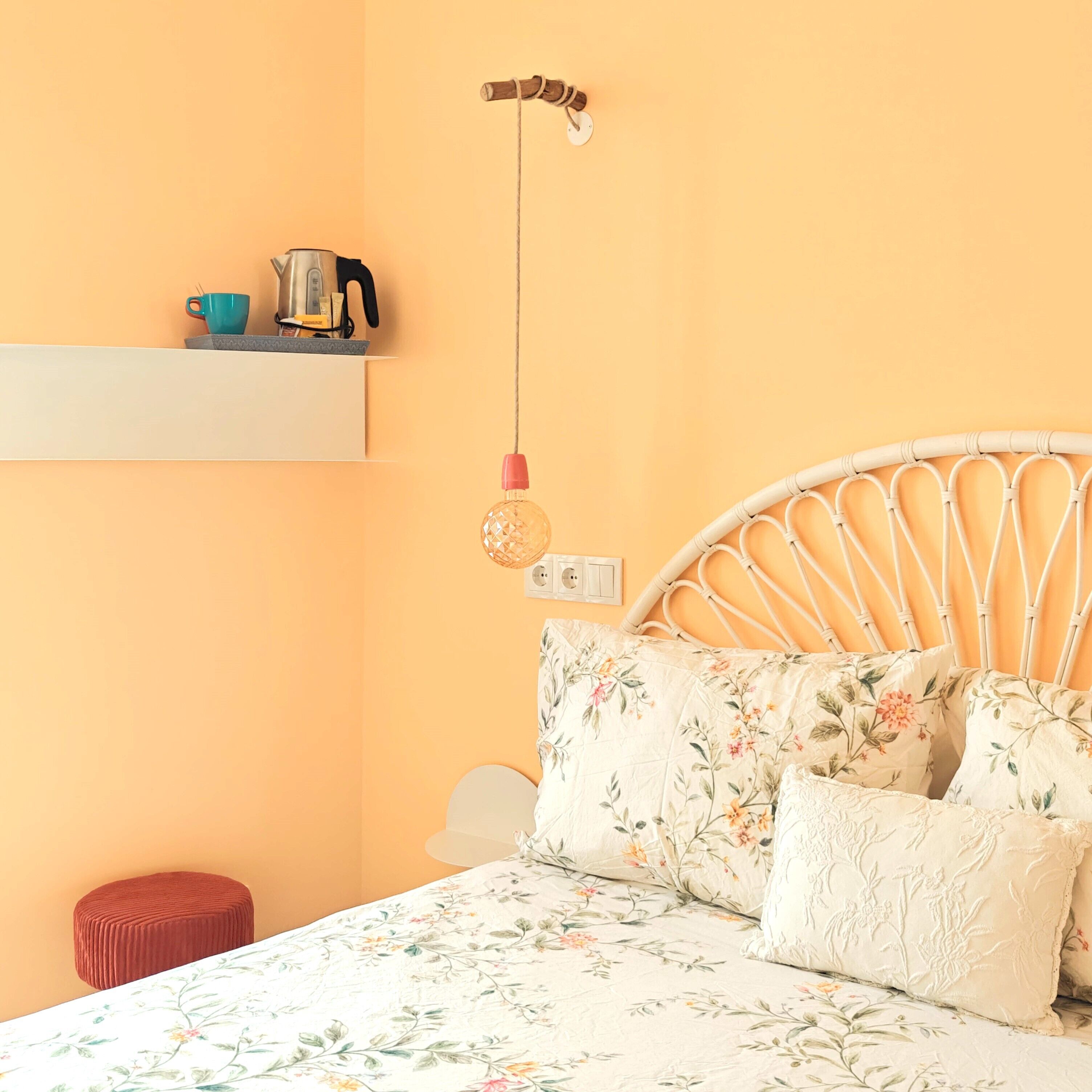 Un lit avec une literie à motifs floraux, une tête de lit en osier et un pouf rouge.
