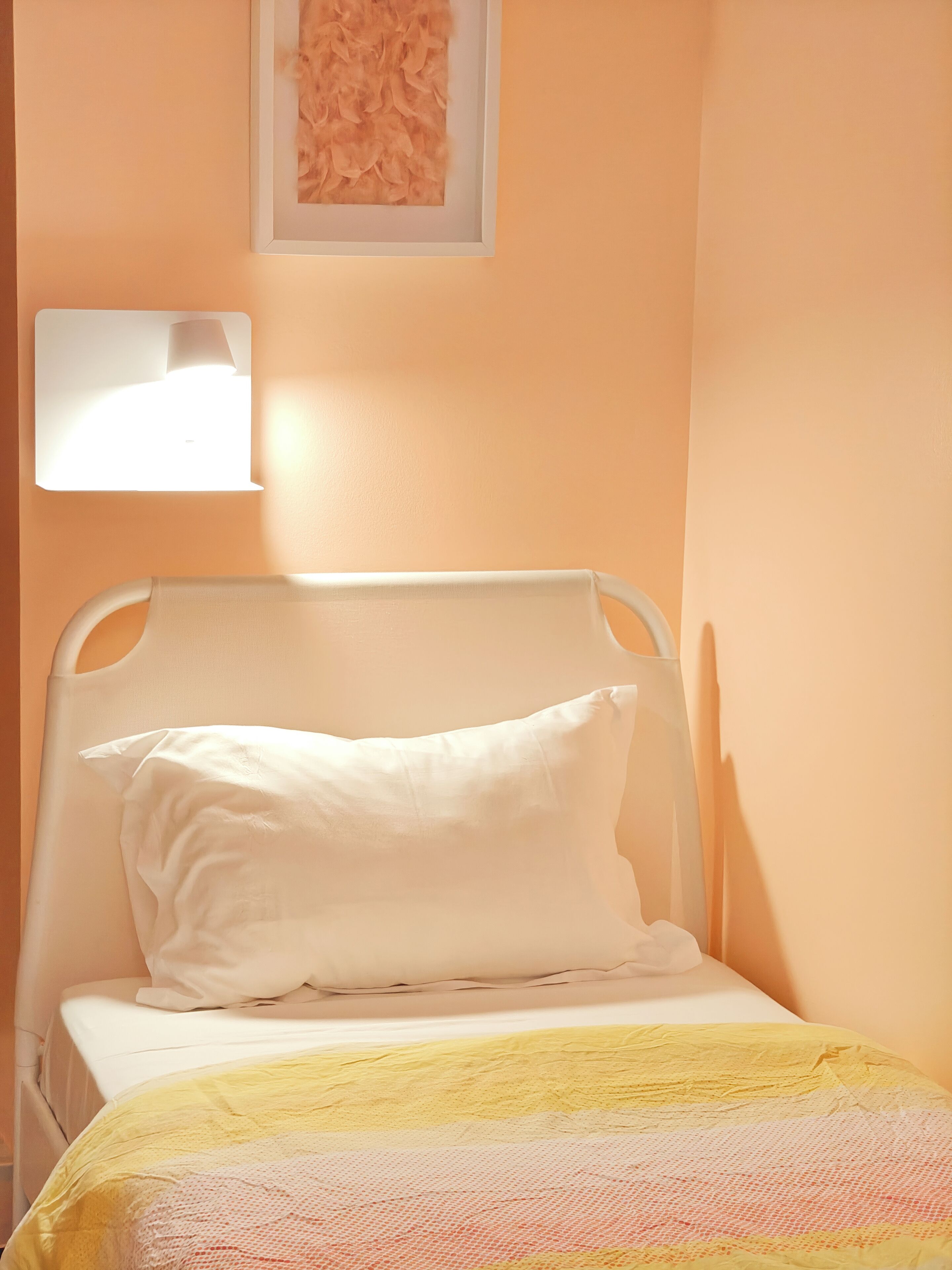 Una cama con cabecera blanca y manta amarilla y rosa.