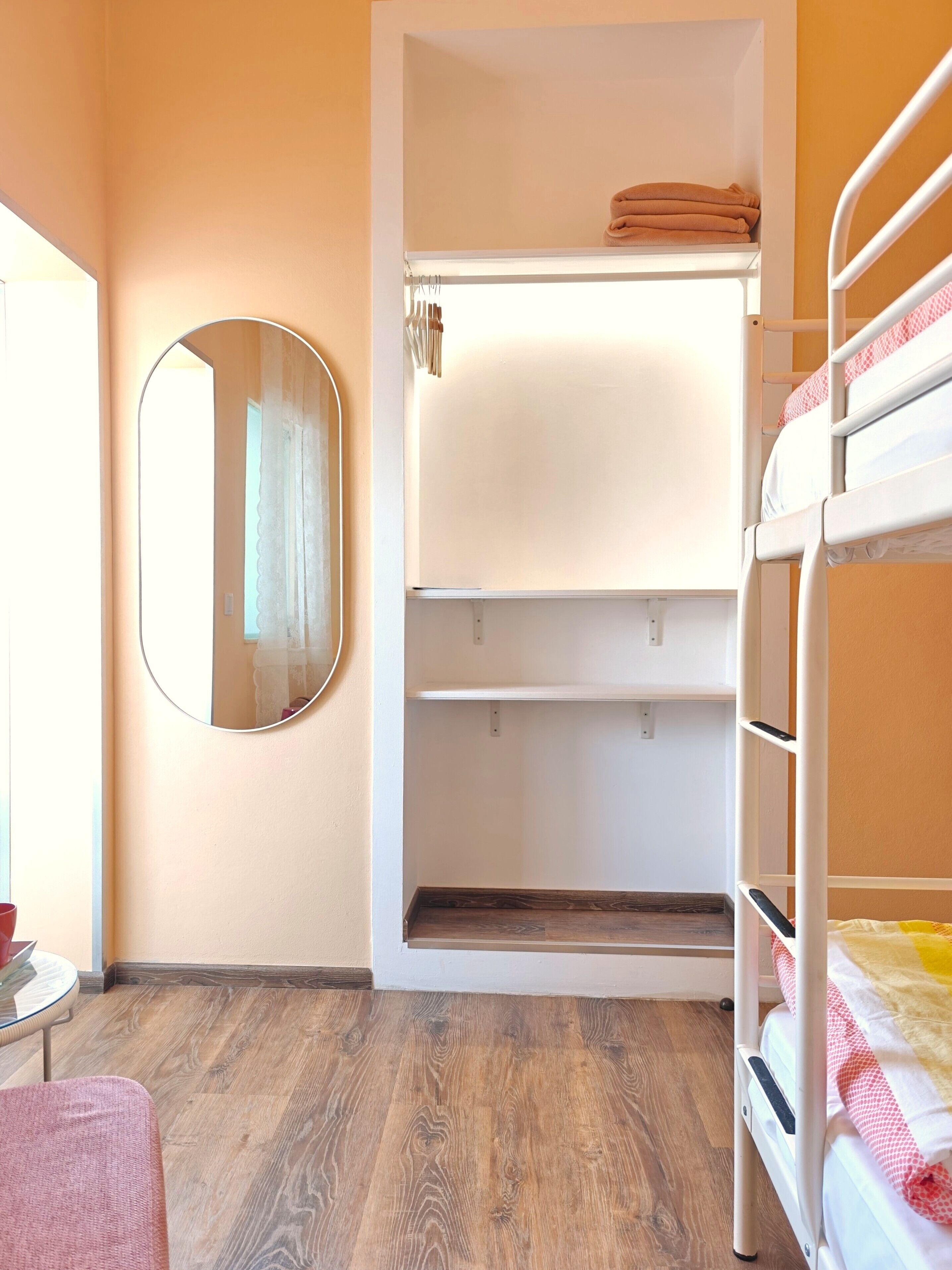 A room with bunk beds, a mirror, and a wardrobe with shelves.