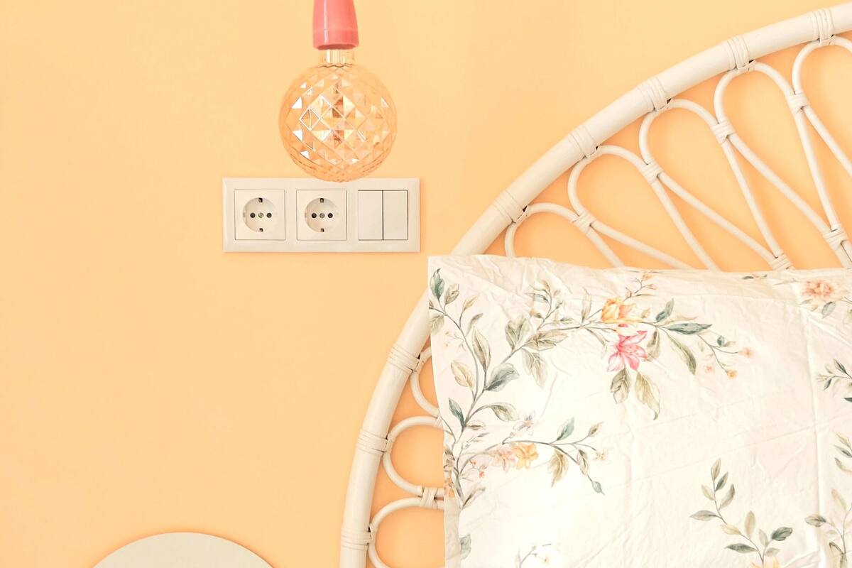 Una cama con colcha estampada, cabecera blanca y lámpara de pared.