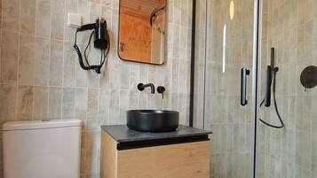Een moderne badkamer met toilet, een wastafel met zwarte waskom, een houten wastafelmeubel, een spiegel en een douchecabine met glazen wanden.