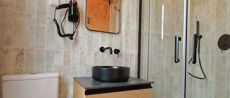 Une salle de bain moderne comprenant des toilettes, un lavabo avec un receveur noir, un meuble-lavabo en bois, un miroir et une douche séparée par une paroi en verre.