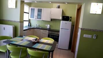 A compact kitchen with a dining area, featuring a refrigerator, stove, microwave, and a sink.