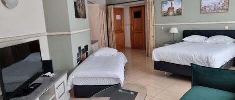 A hotel room with two beds, a TV, a glass table, and a ceiling fan.