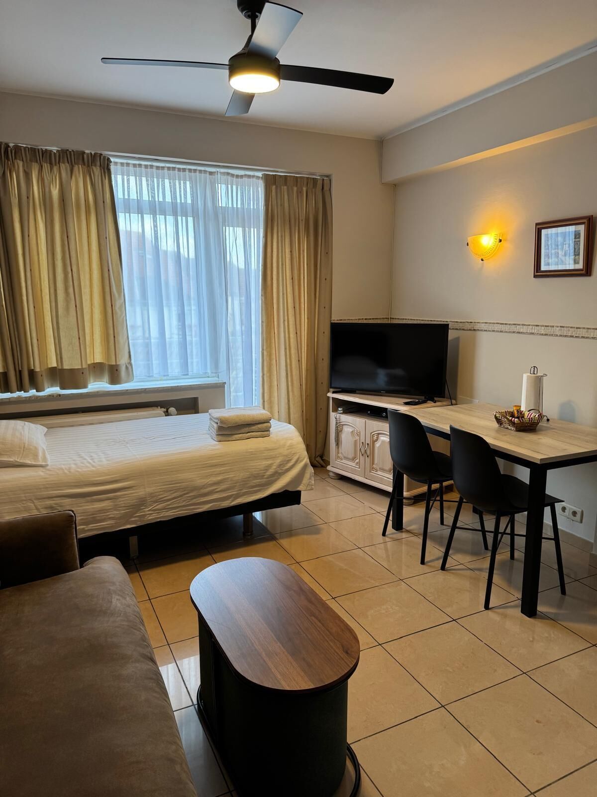 Een hotelkamer met een bed, een bureau, een televisie en een plafondventilator.
